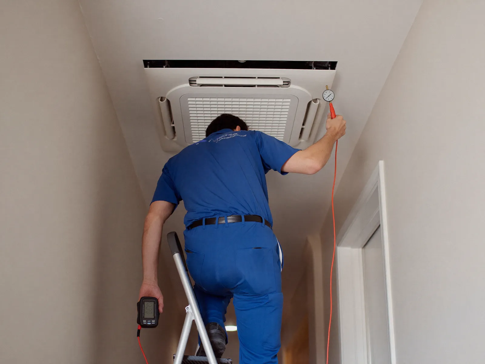 Technician on a ladder checking a ducted AC grille in a townhouse